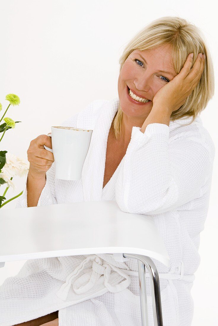 Blonde Frau sitzt mit einer Tasse Cappucchino am Tisch