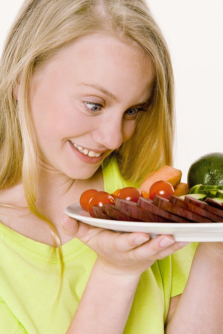 Junges Mädchen schaut auf Gemüseteller in ihren Händen