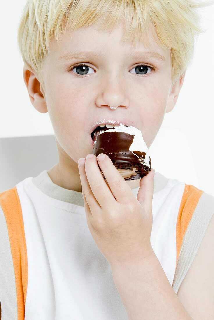 Small boy biting into a chocolate-covered marshmallow wafer