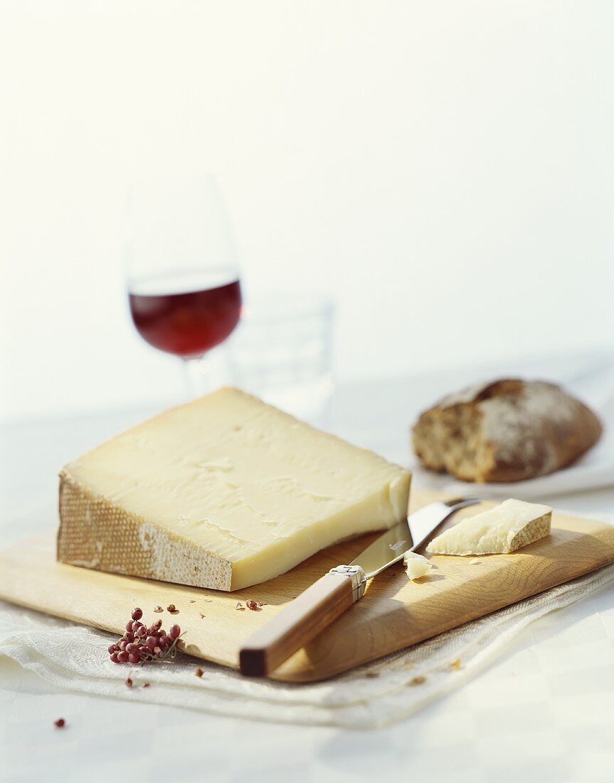 A piece of hard cheese with knife on a wooden board, wine