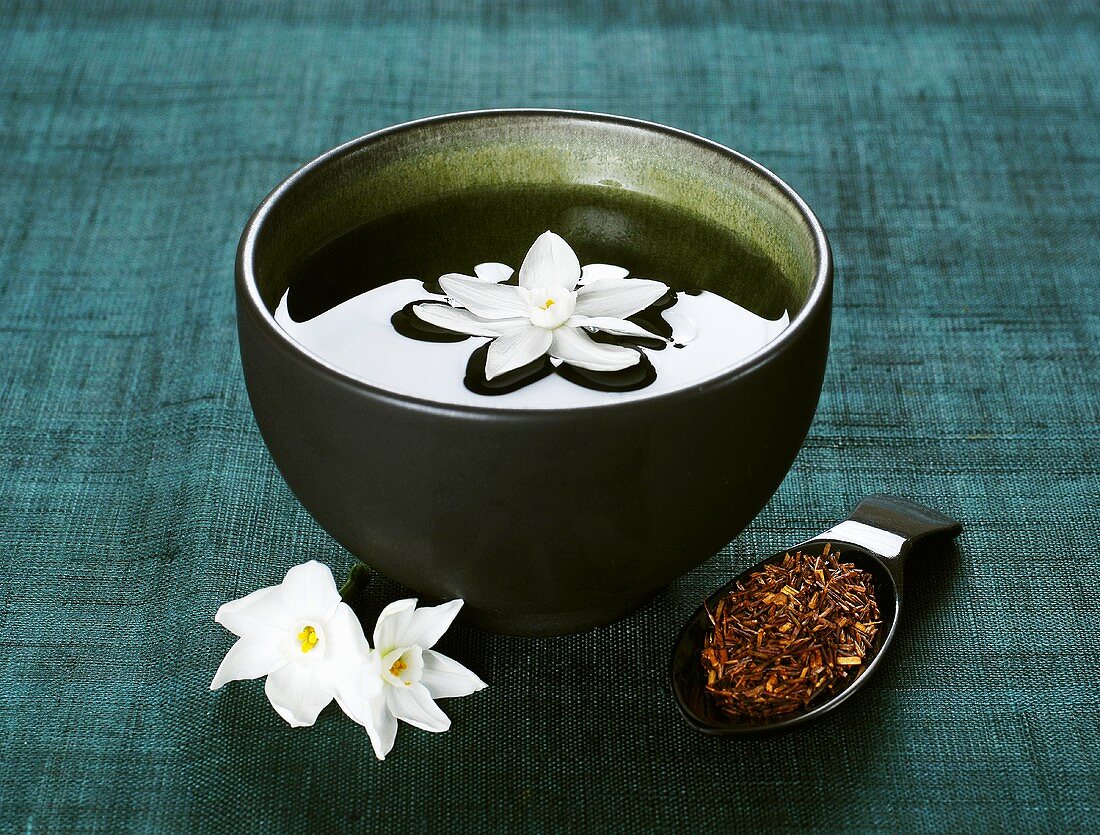 Narcissus flower in bowl of water, tea & flowers beside it