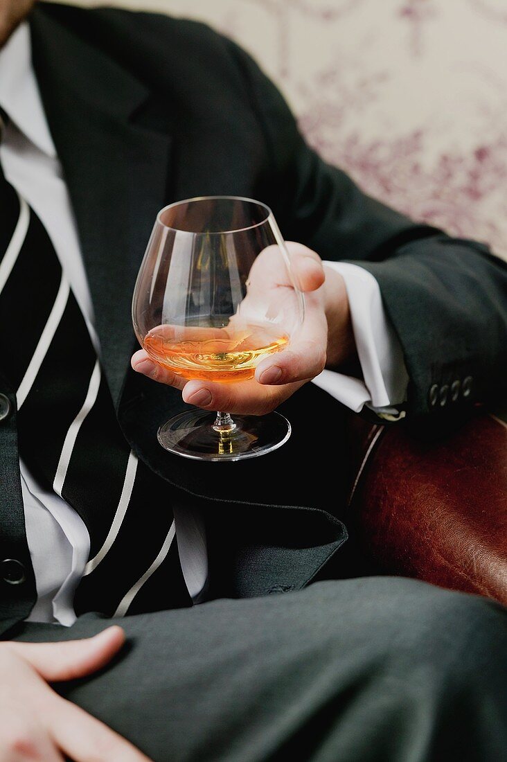 Mann hält ein Glas Cognac in der Hand