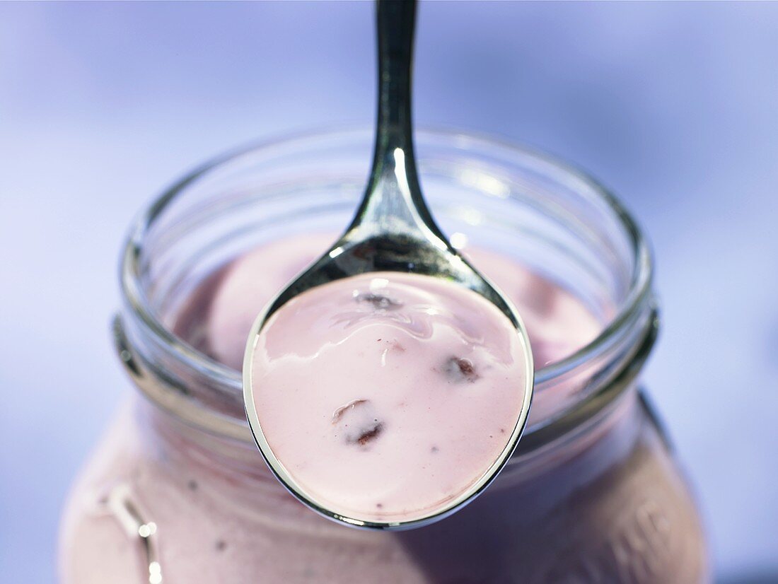 A spoonful of cherry yoghurt on a yoghurt jar