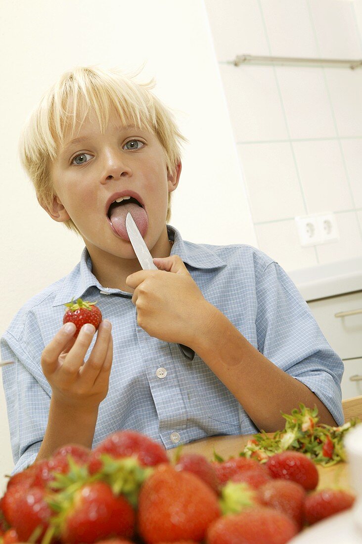 Blonder Junge schleckt Messer ab beim Erdbeeren putzen