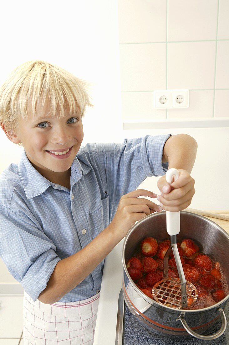 Blond boy crushing strawberries with a potato masher