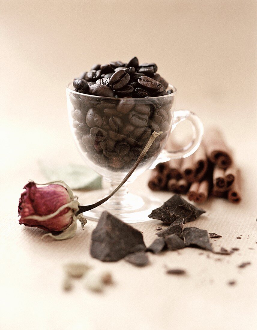 Kaffeebohnen in einem Glas, umgeben von Schokolade und Zimt