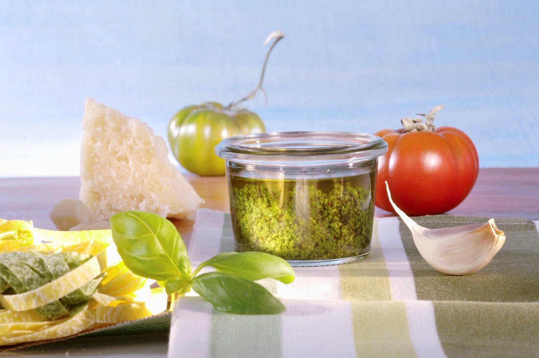 A jar of basil pesto surrounded by ingredients