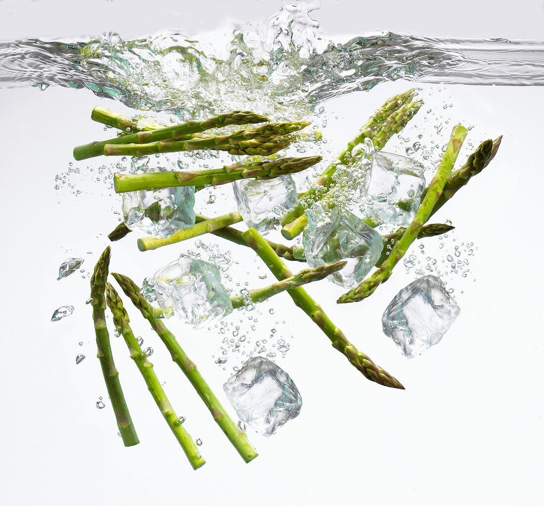 Green asparagus spears and ice cubes falling into water