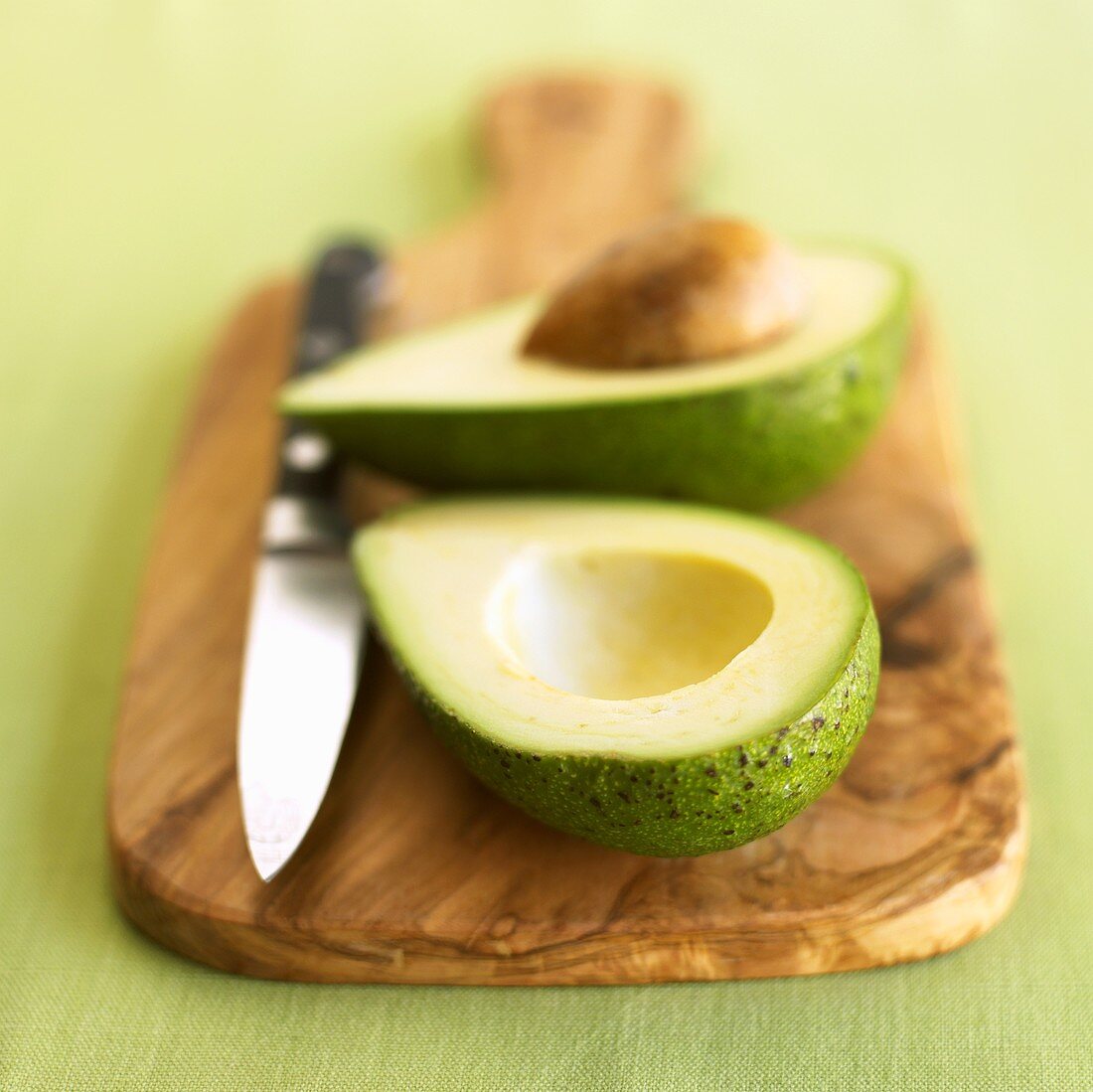 A halved avocado with knife on a wooden board