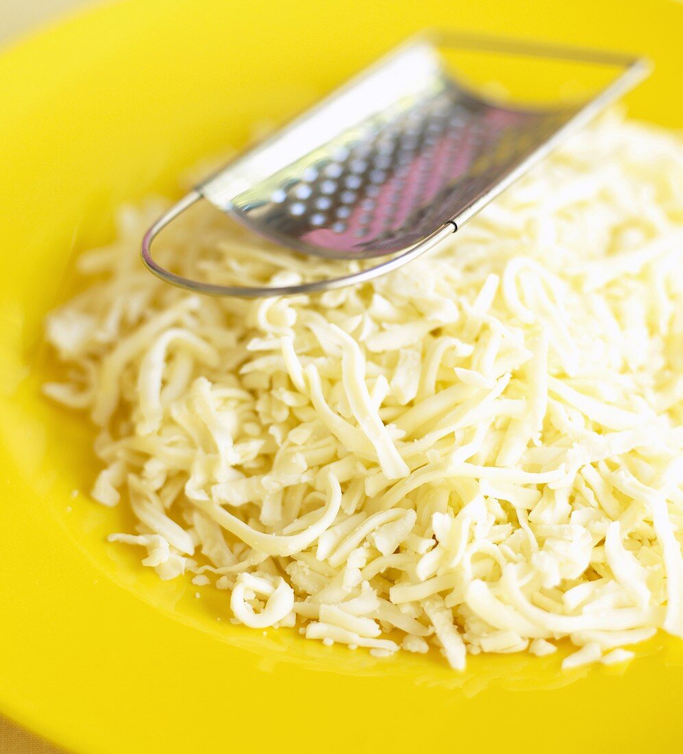 Grated cheese with grater on yellow plate