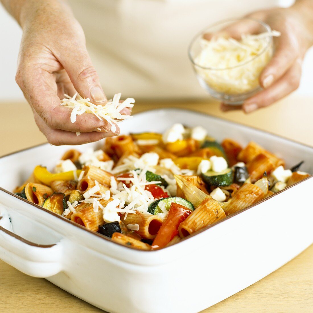 Sprinkling cheese over pasta and vegetable bake