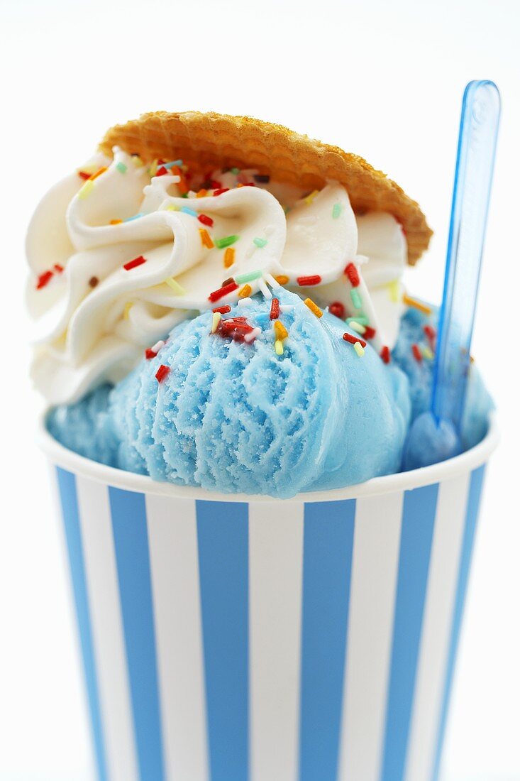 Blue ice cream in tub with sprinkles and plastic spoon