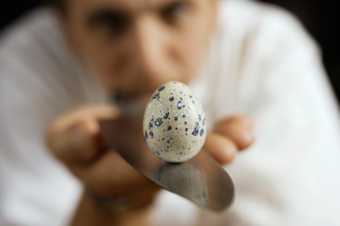 Man balancing a quail's egg on a knife