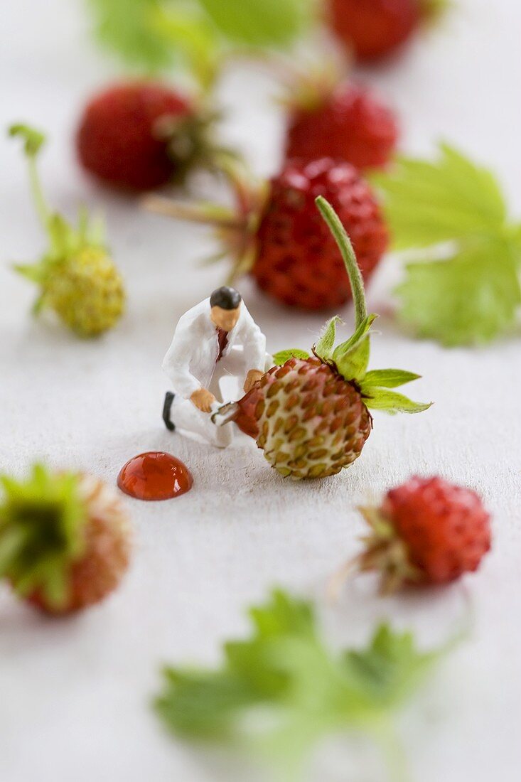 Little toy man among wild strawberries with blob of jam