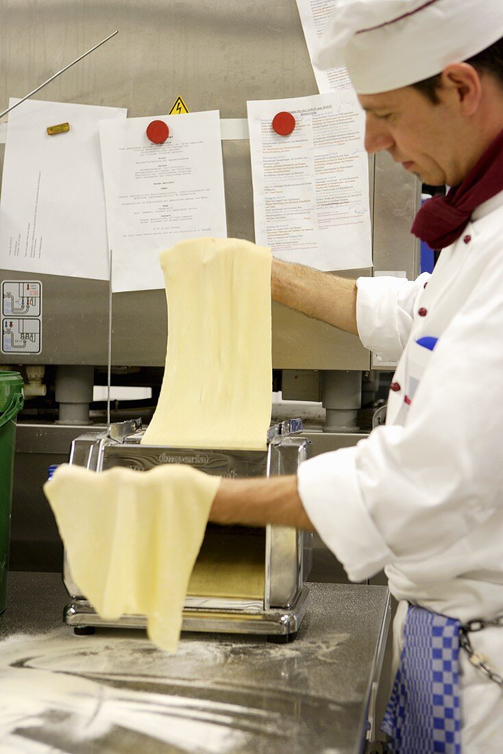 Chef running pasta dough through a pasta maker