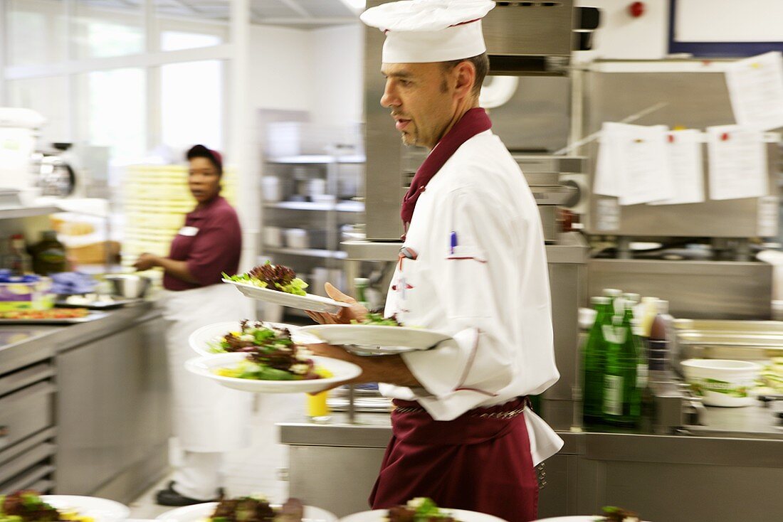 Chef carrying several plates of salad
