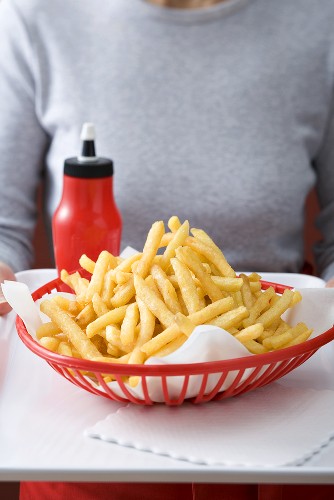 Pommes frites im Plastikkorb, Ketchup, Frau im Hintergrund