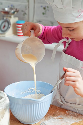 A girl pouring milk into a bowl of flour