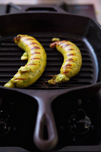 Two vegetable sausages made with zucchini and fennel, frying on a grill pan