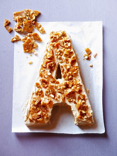 A cake in the shape of the letter A, decorated with nut brittle