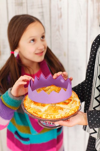 A girl placing a paper crown on a Galette des Rois