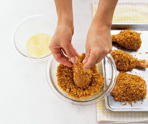 Chicken legs being coated with cornflakes
