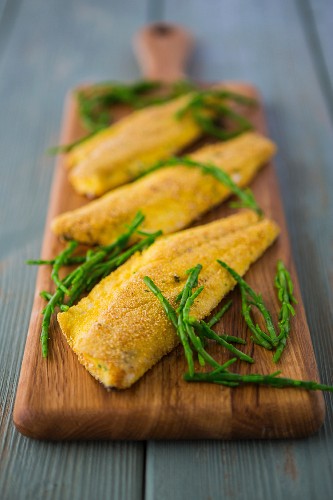 Breaded seabass fillets with a polenta and herb coating, served with samphire on a wooden board