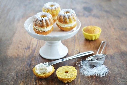 A mini Bundt cake with cream and icing sugar on a cake stand