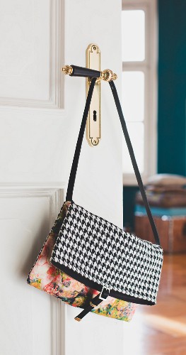 A bi-patterned shoulder bag hanging on a door handle