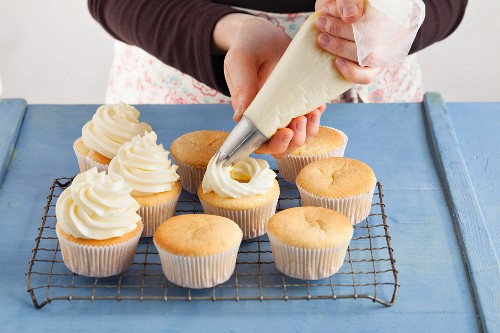 Meringue frosting being piped onto cupcakes