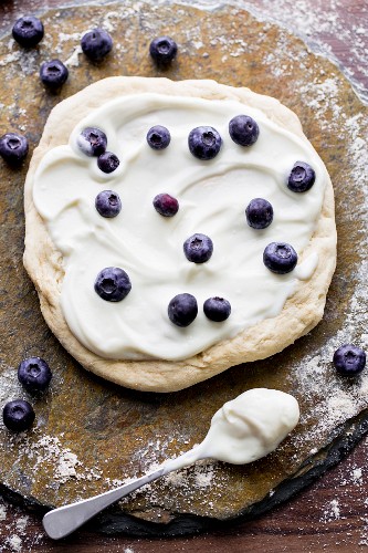 An unbaked pizza with goat's cheese, ham and blueberries