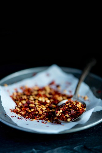 Red Italian chilli flakes on a pewter plate on a white piece of paper