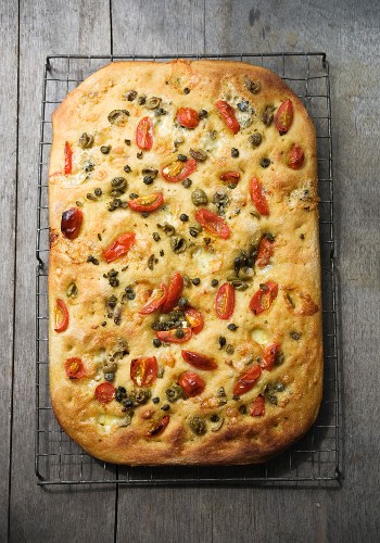 Focaccia topped with tomatoes, capers and olives on a wire rack