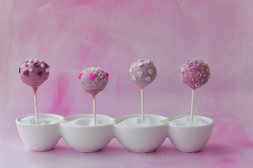 Four purple cake pops in bowls of sugar