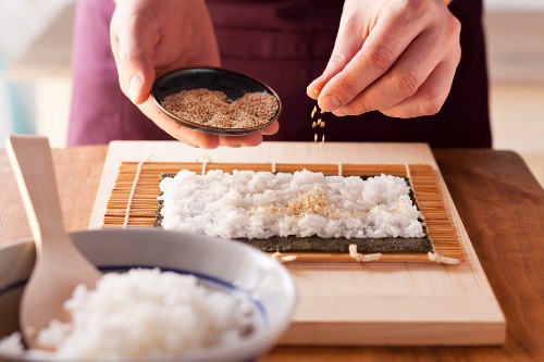 Maki sushi being prepared: rice being sprinkled with sesame seeds