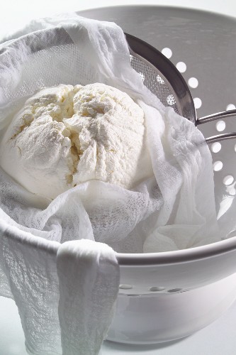 Cream cheese in a muslin cloth and a sieve