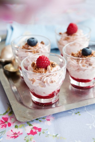A dessert made with cream cheese, biscuits, raspberries and blueberries