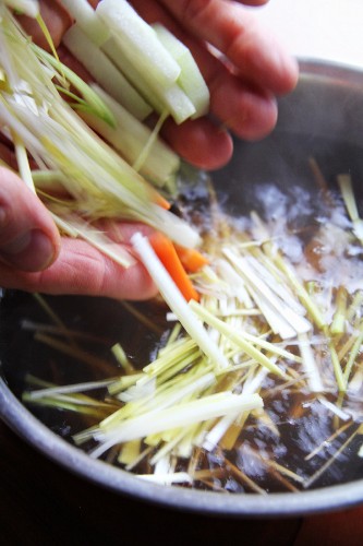Hands adding julienned vegetables to a pot of hot water