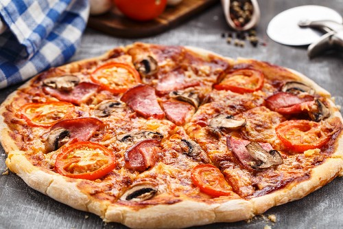 Pizza with tomatoes, ham and mushrooms on a table