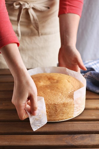 Female hands peeling the parchment paper from the sides of the sponge cake