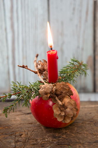 Christmas apple decorated with candle, larch cones and juniper sprig