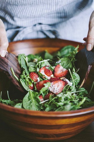 A woman is mixing spinach and arugula to make a strawberry spinach and arugula salad