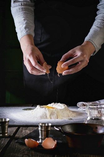 Female hands break the egg into flour for pasta on old wooden kitchen table