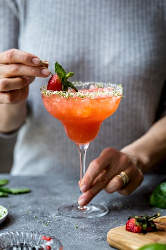 Frau garniert Erdbeer-Champagner-Margarita mit Erdbeerspiesschen