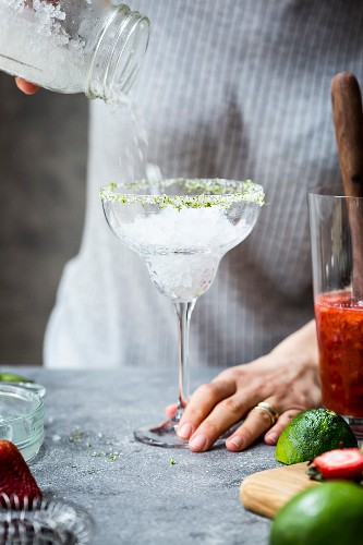 Frau giesst Crushed Ice für Erdbeer-Margarita in Margarita-Glas