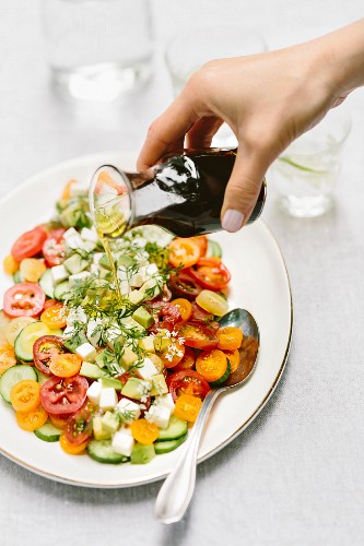Balsamicodressing wird auf Tomatensalat mit Gurken und Mozzarella geträufelt