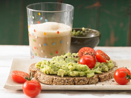 Avocado cream with cherry tomatoes on wholemeal bread served with a glass of cocoa