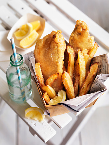 Fish and Chips mit Essig und Zitrone in Papier und Spankörbchen serviert