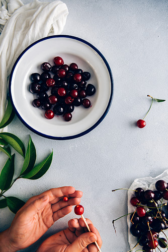 A woman pitting cherries using a wooden skewer on a grey background