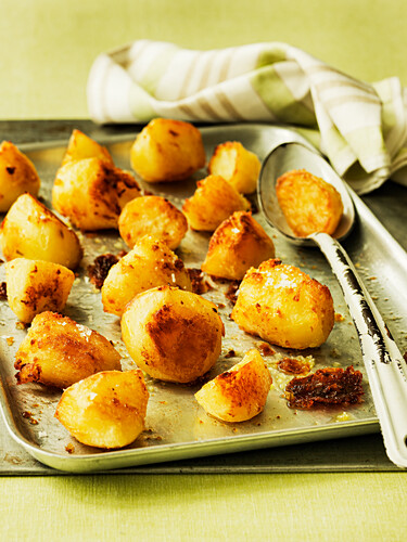 Roasted potatoes with large spoon on a baking tray
